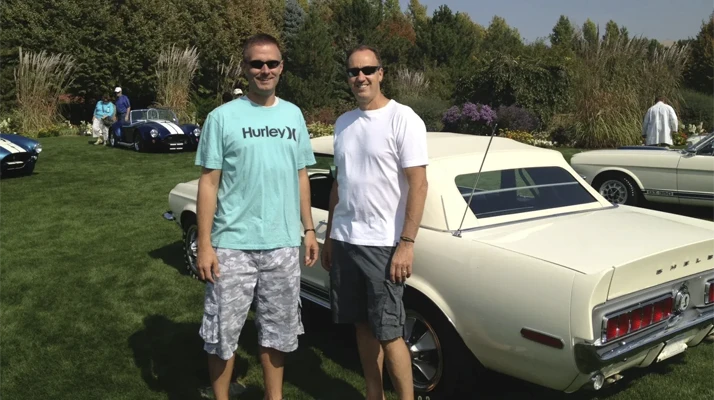 Dr. Lamar C. Fox and Dr. Floyd P. Huxford standing on grass next to a light-colored classic car, with other vintage cars in the background.